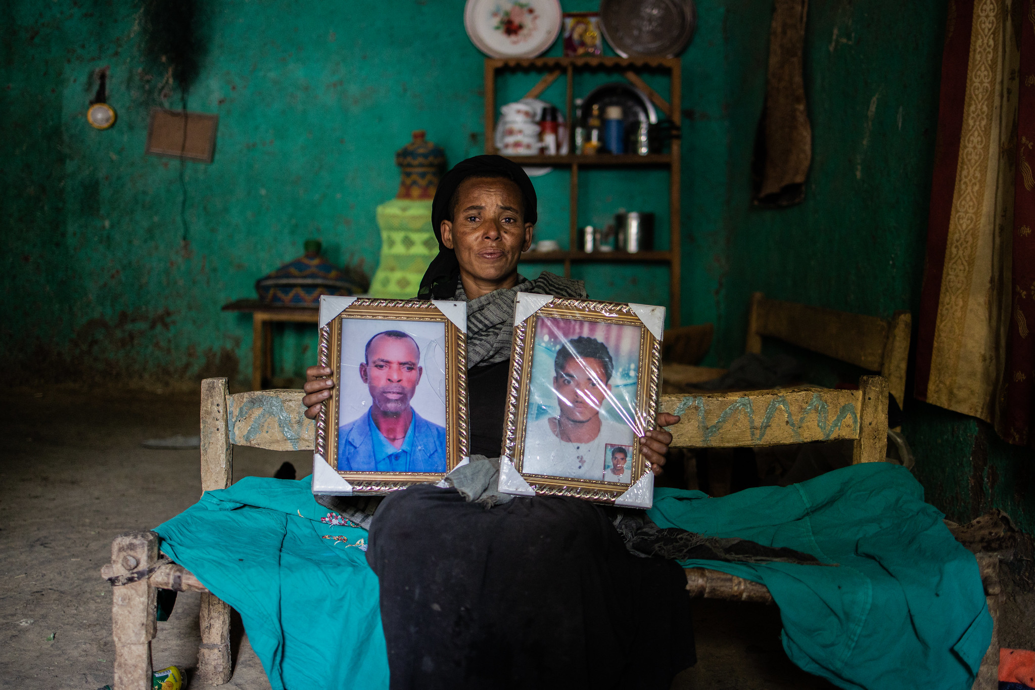 A woman holds two picture frames with photos of two men.