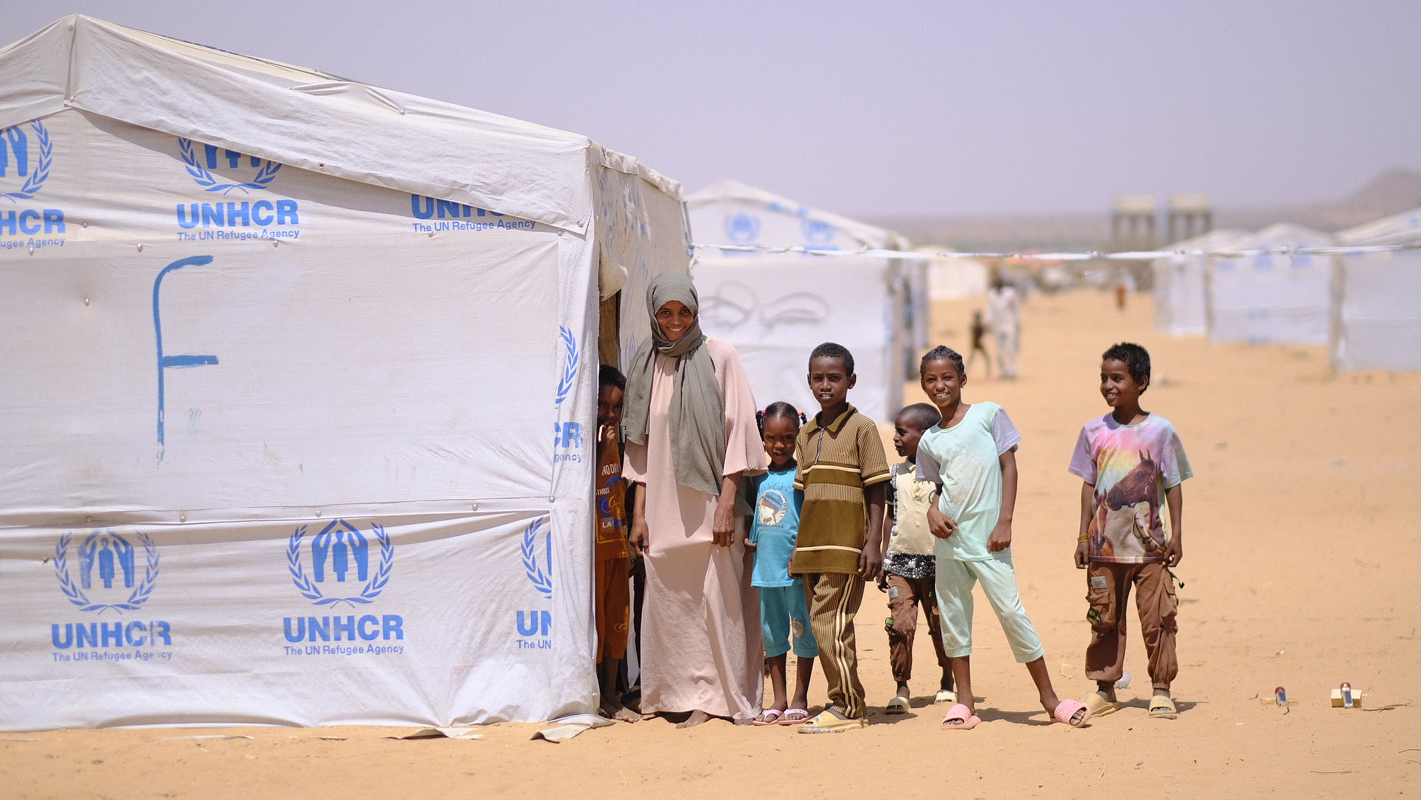 A family stands outside of a temporary shelter with the UNCHR logo on it