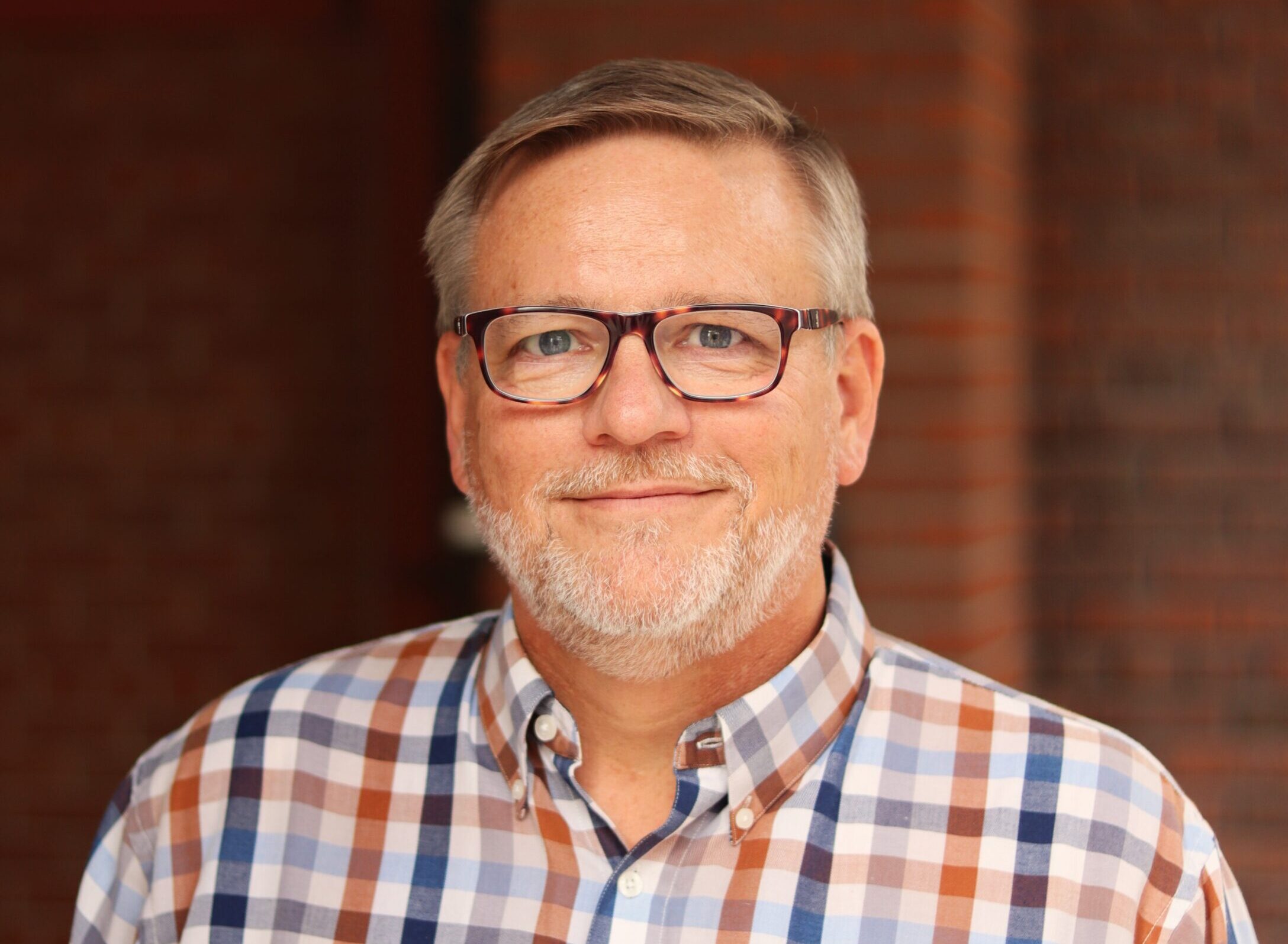 A portrait photo of a main wearing glasses and a checkered shirt